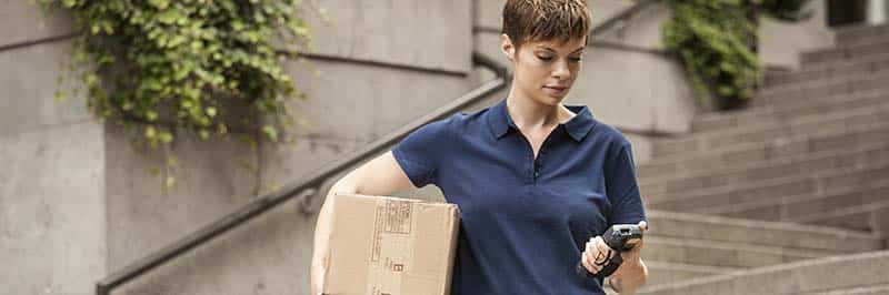 Delivery Woman Carrying Package Down Steps Looking At Handheld Computer