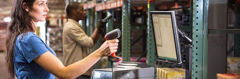 Woman Holding Pistol Grip Barcode Scanner In Front Of Computer Monitor